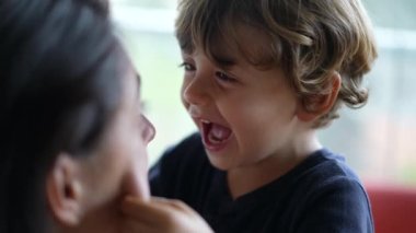  Küçük çocuk anne yanaklarıyla oynuyor. Yakından gülümseyen ve gülen küçük çocuğun yüzü. Oyuncu sarışın erkek çocuk..