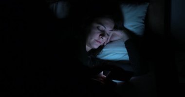 Genç kadın ile smartphone yatakta. Yatmadan önce cep telefonu cihaz oynadığı kadın