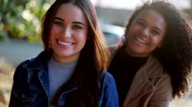 20 'li yaşlarda iki farklı kadın dışarıda gülümsüyor.