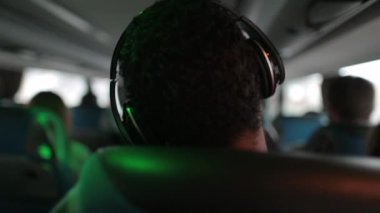 Kulaklık takan bir adam otobüsle seyahat ederken müzik dinliyor.