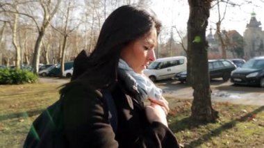 Soğuk mevsimde parkta ağır çekimde yürüyen bir kadın. Kadın yürürken paltosunu ve saçını düzeltiyor.