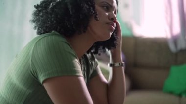 Düşünceli siyah bir kadın evde kıvırcık saçlarıyla oynuyor. Afrikalı Amerikalı kız saçlarıyla oynuyor.