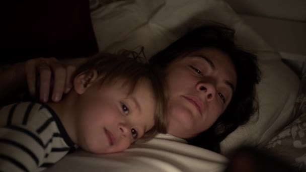 母と子供はベッドで寝そべって夜にスマートフォンを見て — ストック動画