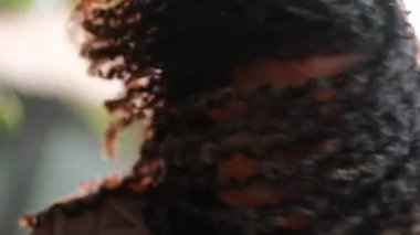 Genç siyah, kıvırcık saçlı, saçları ağır çekimde hareket eden melez bir kadın.