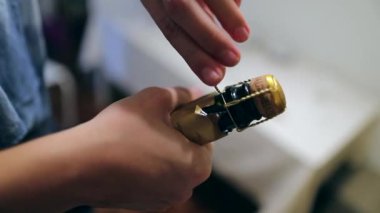 Şampanya mantarı iten ellerin yakın çekimi. Kadın şampanya şişesini açıyor.