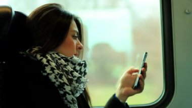 Kadın trende giderken cep telefonu teknolojisine bakıyor.