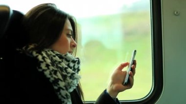 Kadın trende giderken cep telefonu teknolojisine bakıyor.