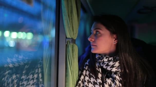 女性は夜バスで旅行する 女の子は夜にバスの窓の外を見る都市の景色が通り過ぎるのを見る — ストック動画