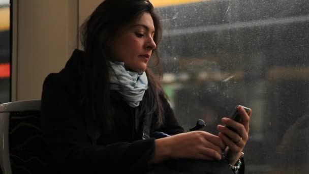 女性は電車の中で携帯電話の装置を見ている トラムに乗っている間に彼女のスマートフォンをチェックする通信 — ストック動画