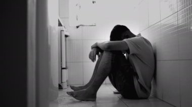 Depresyondaki genç adam, tek renkli zor zamanlarda mutfak zemininde otururken yüzünü kapatıyor. Akli dengesi bozuk bir erkek. Stres negatif duygular