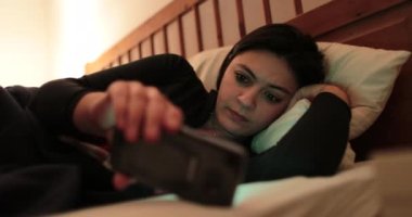 Genç kadın ile smartphone yatakta. Yatmadan önce cep telefonu cihaz oynadığı kadın