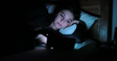 Genç kadın ile smartphone yatakta. Yatmadan önce cep telefonu cihaz oynadığı kadın