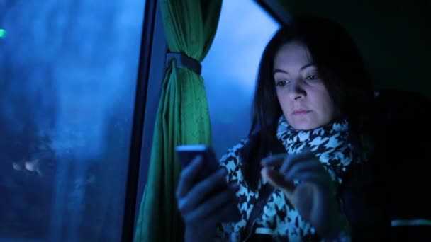 窓の横のバスで移動しながら 夜に携帯電話のデバイスを使用して女性 女の子は移動中に友人に電子メールやテキストメッセージをチェック車両 — ストック動画