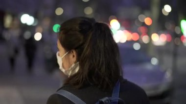 Gece vakti şehirde gezen yüzü maskeli genç bir kadının arkası.