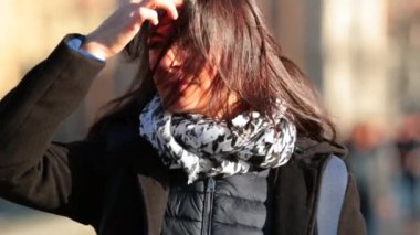 Kadın saçlarını şehrin sokaklarında soğuk kış mevsiminde 4K 60fps yavaş çekimde yürürken düzenliyor. Gün batımında kaldırımda yürüyen kadın