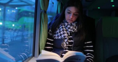 Gece otobüsle seyahat eden yolcu kadınların kitap okurken 4K 'lık gizli bir videosu. Kız akşamları pencerenin yanındaki hareket halindeki bir araçla hikaye okur.