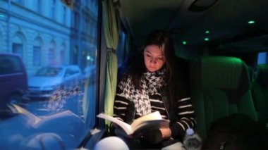 Akşamları otobüsle seyahat eden bir kadın. Hareket halindeyken kitap okuyan kız
