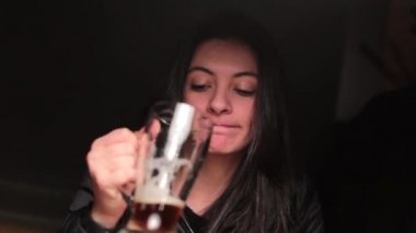 Mutlu kadın yarı boş bira içiyor, kameraya bakıyor ve gülümsüyor..