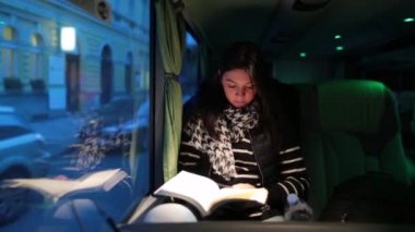 Akşamları otobüsle seyahat eden bir kadın. Hareket halindeyken kitap okuyan kız