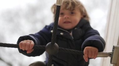Küçük çocuk oyun parkındaki ekipman kablosuna tırmanıyor.