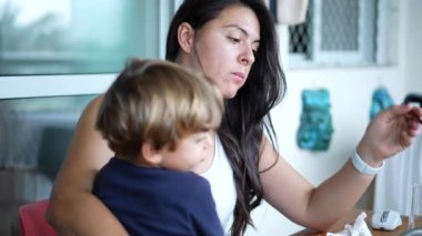 Diğeri kucağında çocuk varken yemek yiyor. Annesi küçük çocuğu çatalla besliyor..
