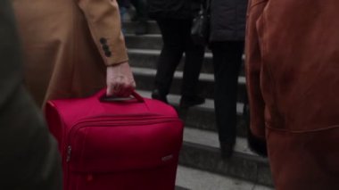Kalabalık bir yerde merdivenlerin yukarısında büyük kırmızı bavulu önemseyen biri.