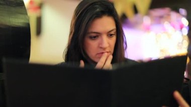 Restoran menüsünü tutan kadın. Kafe restoranında oturan kızın menüsünü gösteren gizli bir klip.