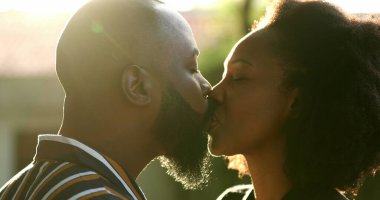 Siyahi bir adam dışarıda mercekli güneş ışığıyla karısını öpüyor. Afrikalı çiftler sevgi ve sevgi