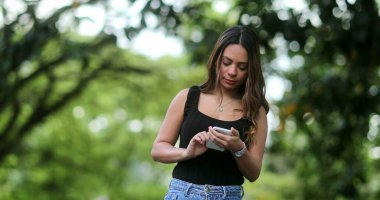 İspanyol Brezilyalı kadın doğada cep telefonu ekranına bakıyor.