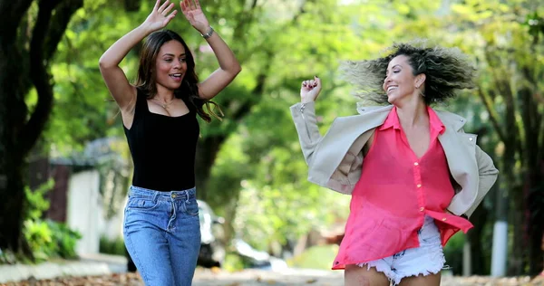Happy people dance outside in street, two female friends celebrating life dancing