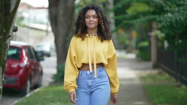 1つの幸せなブラジルの若い女性の街の笑顔を歩く 20代のアフリカ系アメリカ人の少女が歩道を歩いています — ストック写真