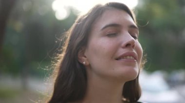 Meditasyon yapan genç bir kadın derin derin göz kapayarak doğada dikiliyor.