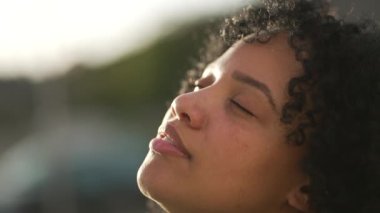 Meditasyon yapan genç bir kadın gökyüzüne gülümseyen gözlerini açıyor. Düşünceli, İspanyol, Brezilyalı bir kadın kendini özgür hissediyor.