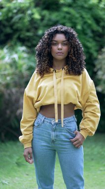 20 'li yaşlarda Latin kökenli genç bir kız dışarıda kameraya bakıyor. Dikey Video 'da kıvırcık saçlı ve sarı bluzlu Afro-Amerikan kadın.