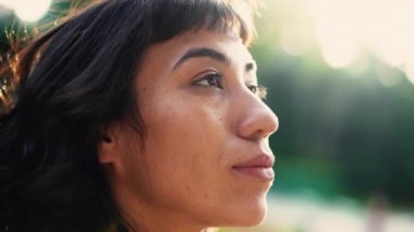 Güney Amerikalı genç bir kadının profil profili güneş ışığında mercek patlaması ile dışarıda duruyor. Ciddi bir ifadeyle Latin kıza yakın dur.