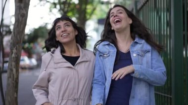 İki neşeli, mutlu ve dışa dönük genç kadın dışarıda yürürken gülüyor ve gülümsüyor..