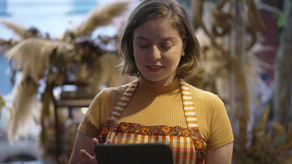 Young female employee holding tablet checking inventory at small business store warehouse for online delivery. Staff at Flower Shop shopYoung female employee holding tablet checking inventory at small business store warehouse for online delivery. Sta