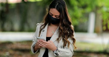 Kapalı maskeli bir kişi dışarıda cep telefonu kullanıyor.