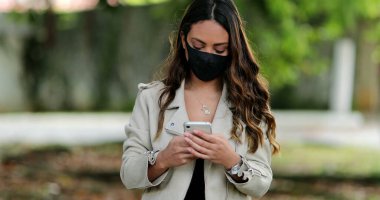 Kapalı maskeli bir kişi dışarıda cep telefonu kullanıyor.