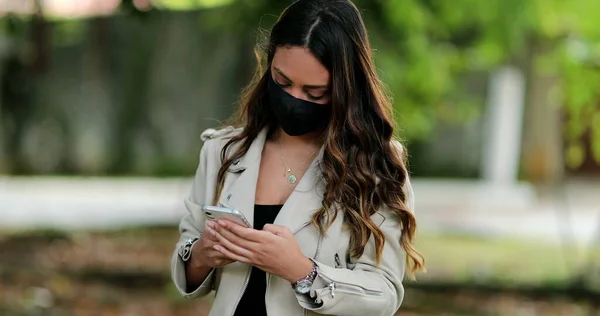 Person wearing covid mask using cellphone outside