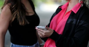 Dışarıda cep telefonu ekranına bakan iki kadın.