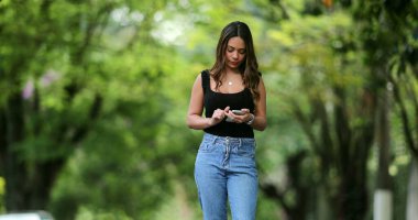 Sokakta akıllı telefon cihazına bakan genç melez bir kadın.