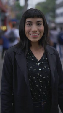 Şehir kaldırımında durup gülümseyen kameraya bakan mutlu kadın. Dikey Videodaki Güney Amerikalı Latin kadın