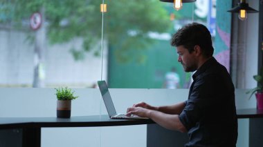 Genç adam dizüstü bilgisayarı açıyor. Şehir kaldırımlarında uzaktan kumandayla çalışıyor. Modern teknoloji aygıtı kullanan kişi