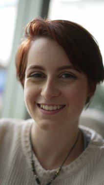 Dikey videoda kameraya gülümseyen kızıl saçlı genç bir kadının portresi. Mutlu 20 kız SS 'e bakıyor.