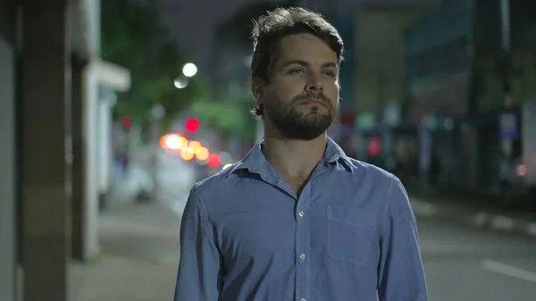 Pensive young man walking in city street at night. Thoughtful person walks in urban sidewalk in mental reflection in the evening