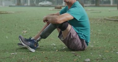 Orta yaşlı, sakat erkek bir sporcunun portresi. Protez bacaklı, dışarıda oturmuş parkta gülümsüyor.