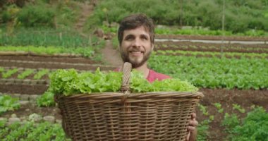 Yerel çiftlikte kameraya gülümseyen organik marul sepeti tutan genç bir adamın portresi. Gıda ve sürdürülebilirlik kavramı