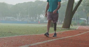 Orta yaşlı engelli bir atletin ön görüntüsü protez bacaklı bir sporcunun koşan pistte kameraya doğru yürümesi.