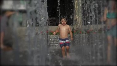 Su parkında ağır çekimde 240 fps hızla koşan mutlu küçük çocuk. Küçük bir çocuk sıcak yaz günü taze bir çeşmede koşar.